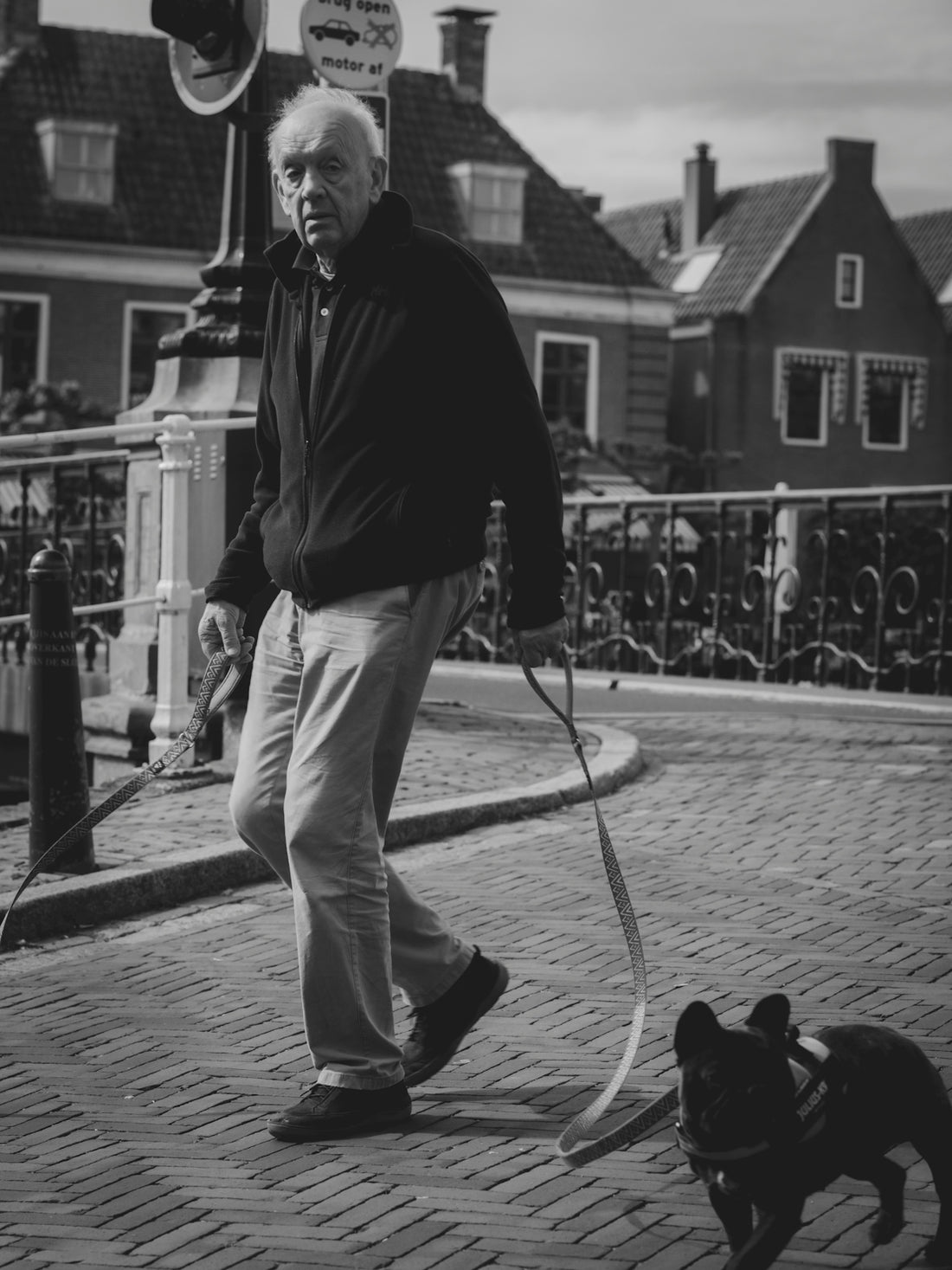 Elderly man walking a small dog on a cobblestone street.