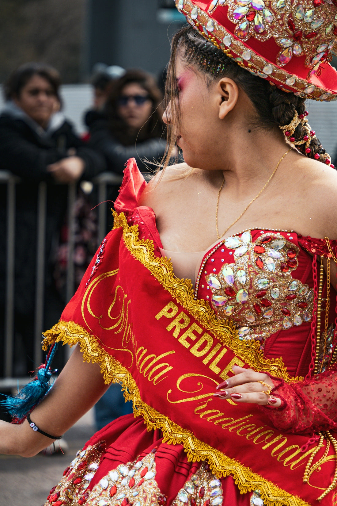 A woman in a red sequined costume with a sash at a parade.